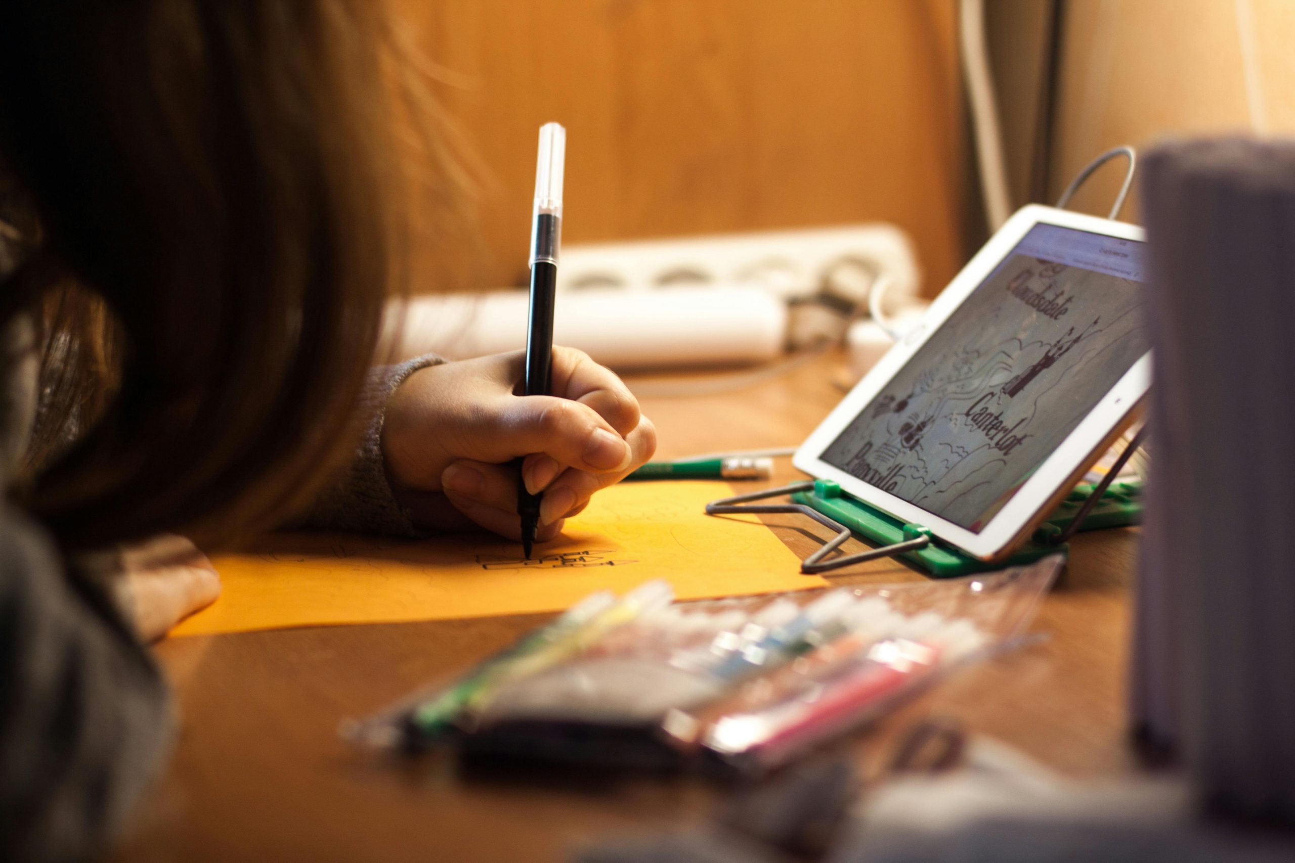 A young girl drawing at a desk with a tablet for reference, highlighting creative use of technology.