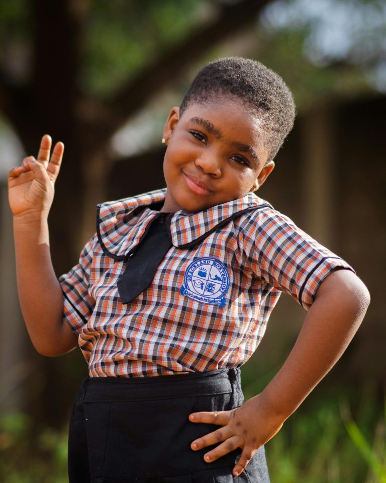 Charming young girl in school uniform confidently posing outdoors, expressing joy and pride.