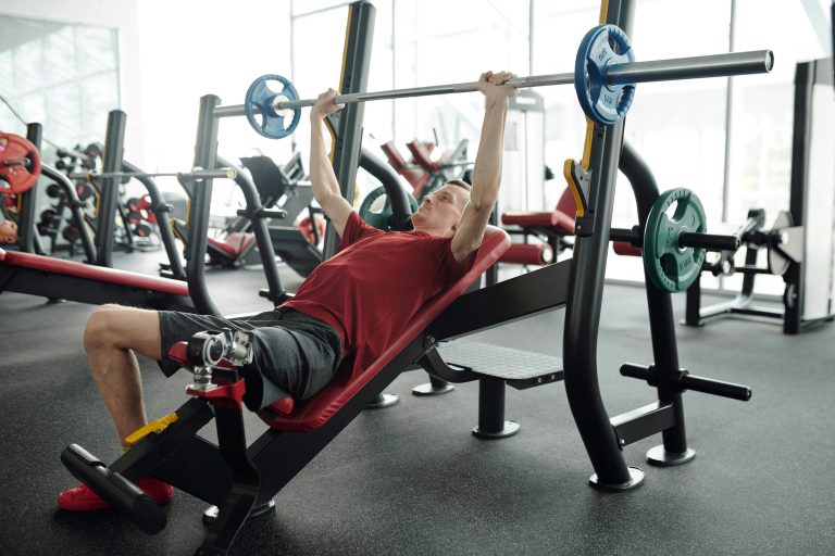 A man with a prosthetic leg lifting weights on an incline bench in a gym setting.