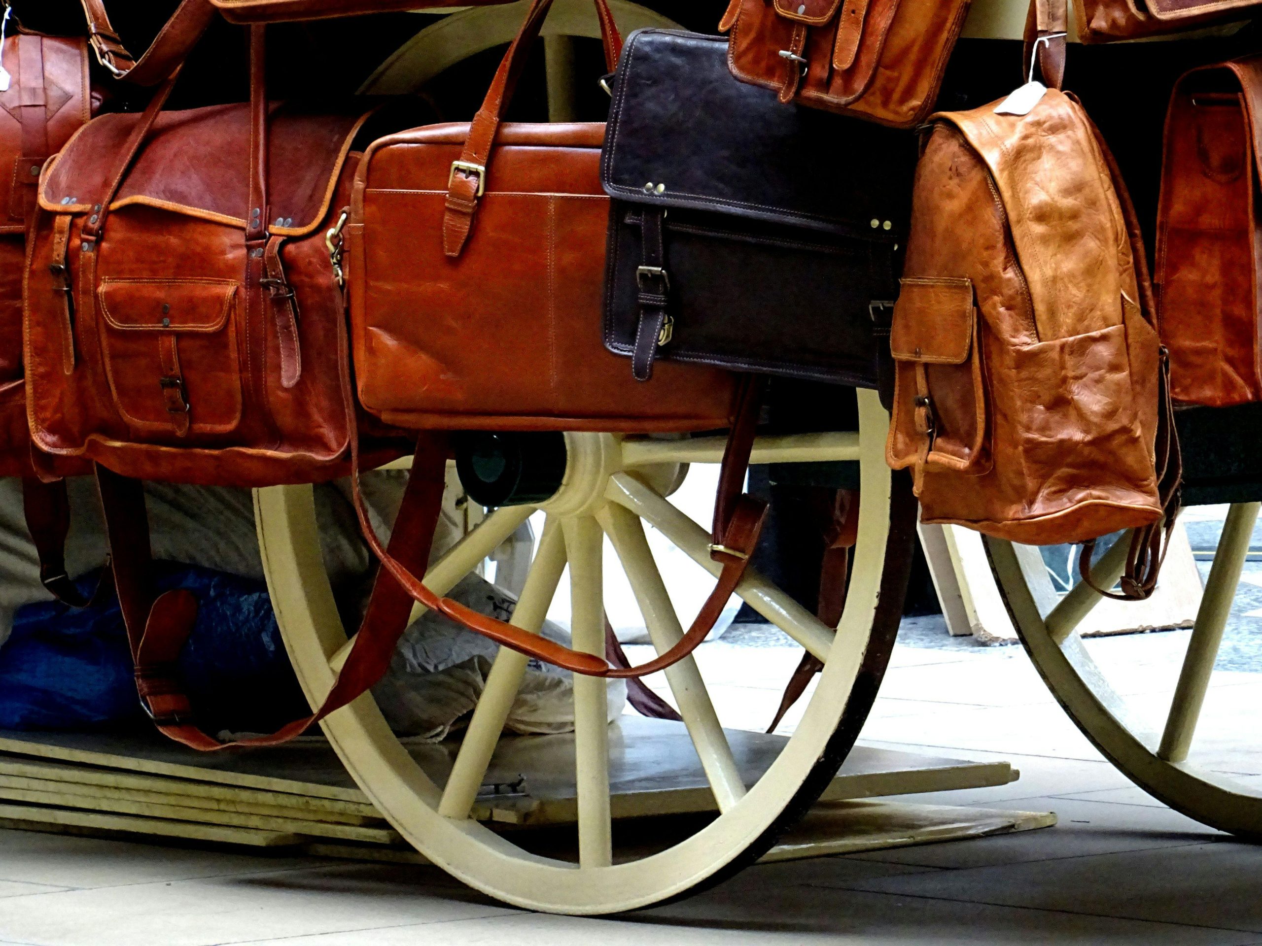 A variety of leather bags elegantly displayed on a classic wooden carriage wheel.